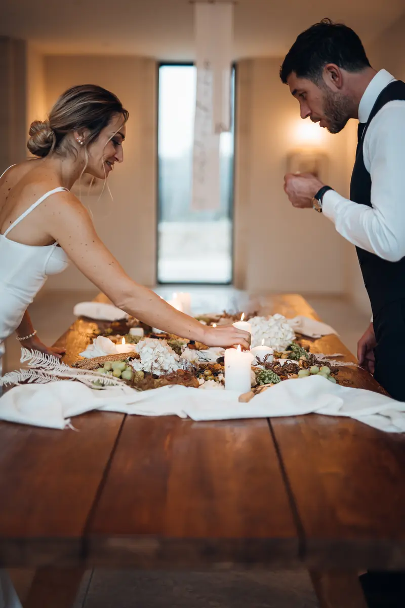 Les mariés penchés sur une longue table en bois garnie et éclairée de bougies, Mon Petit Pâturage